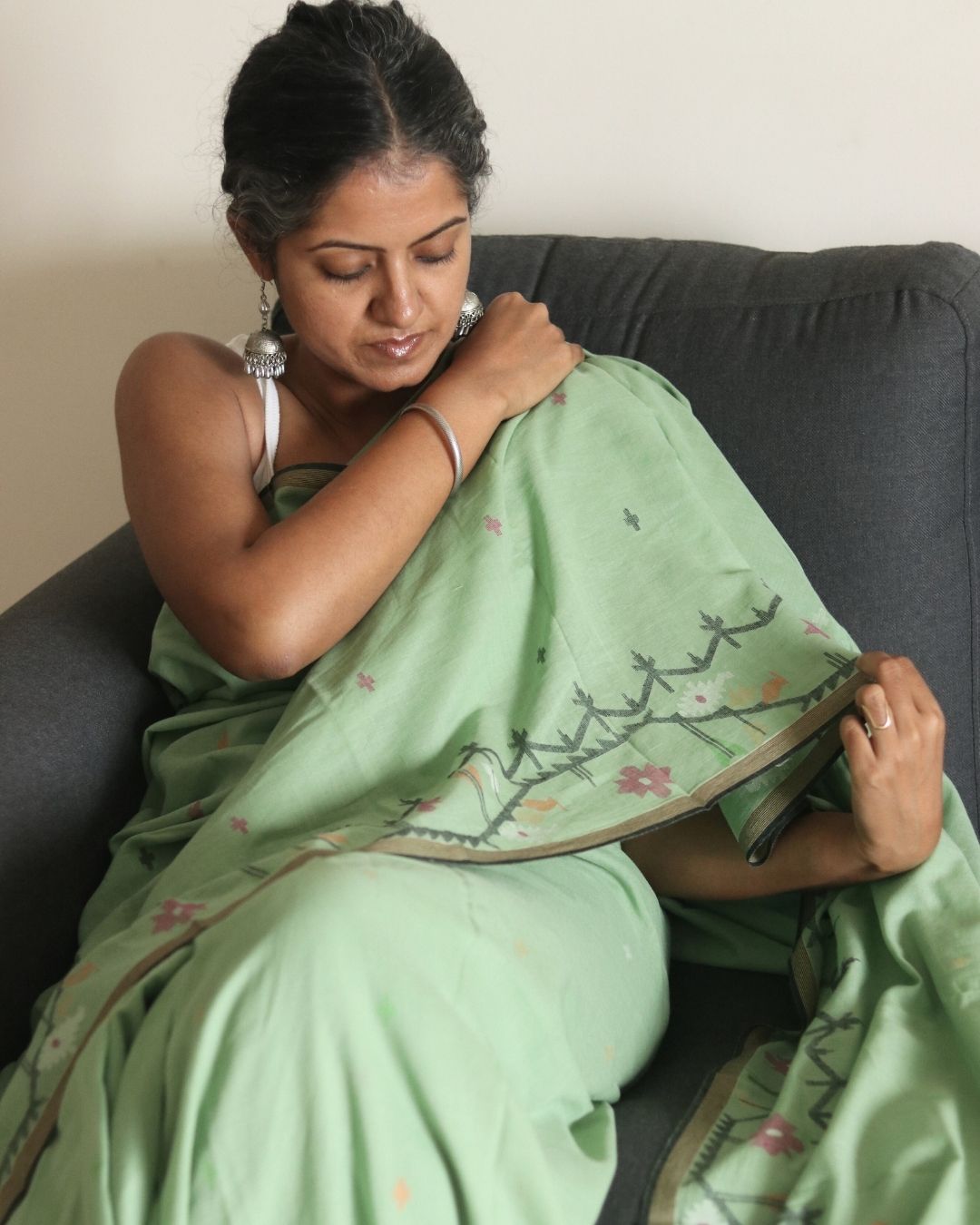 A woman wrapped in a soft green handwoven Bengal cotton saree with delicate woven motifs, highlighting traditional weaving techniques and breathable fabric — an elegant, lightweight saree ideal for everyday wear and relaxed styling.