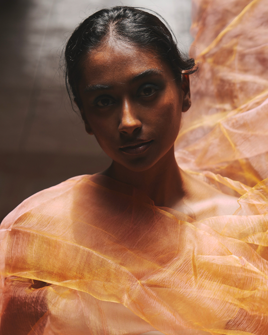 Model draped in the Sunburst Pink handwoven silk scarf, highlighting its feather-light texture and luminous colour play. Crafted using traditional handloom techniques, this luxury silk scarf shifts beautifully between golden and pink tones, embodying timeless artisanal craftsmanship and contemporary elegance.