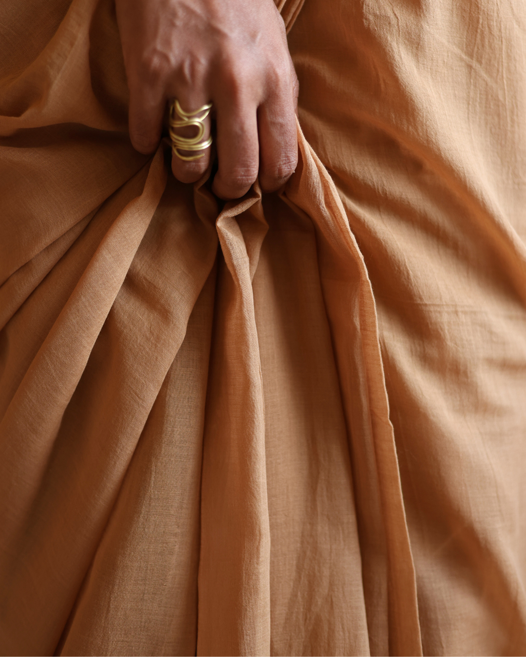 Close-up of the DUNE handwoven cotton saree in a warm desert sand hue, showcasing its soft pleats and natural drape. The earthy brown-beige fabric captures the texture and movement of shifting dunes, blending timeless craftsmanship with contemporary minimalism — perfect for everyday wear or understated elegance.