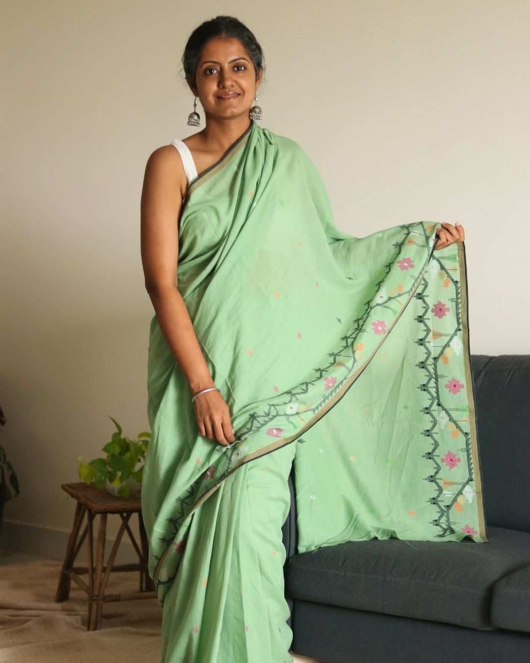 Model wearing a handwoven light green Bengal cotton saree with floral motifs and a detailed woven border, showcasing the soft drape, lightweight texture, and traditional craftsmanship of the fabric. Perfect for everyday wear, casual gatherings, or cultural occasions.
