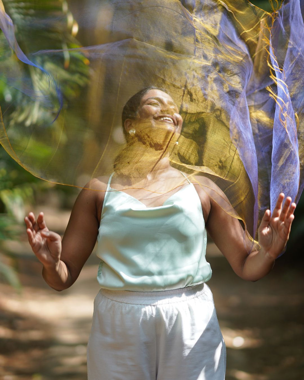 Woman in a light green top and white pants standing outdoors with a blurred natural background