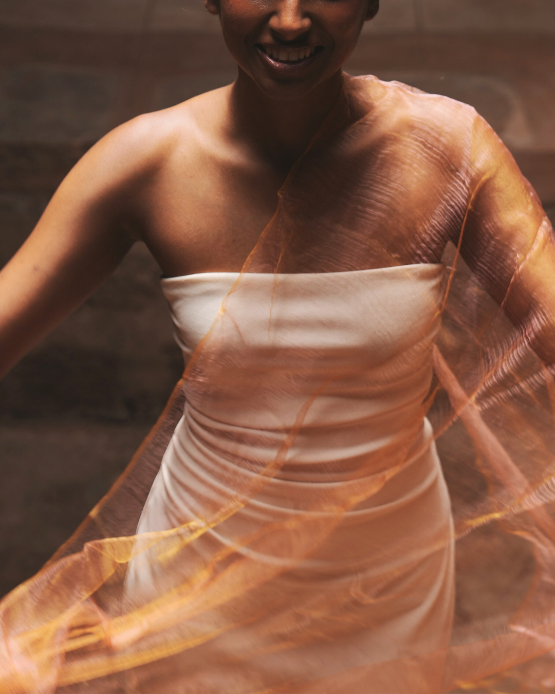 Sunburst Pink luxury handwoven silk scarf draped across a strapless white dress – lightweight, sheer, colour-shifting artisan scarf for women, styled as an elegant statement accessory.