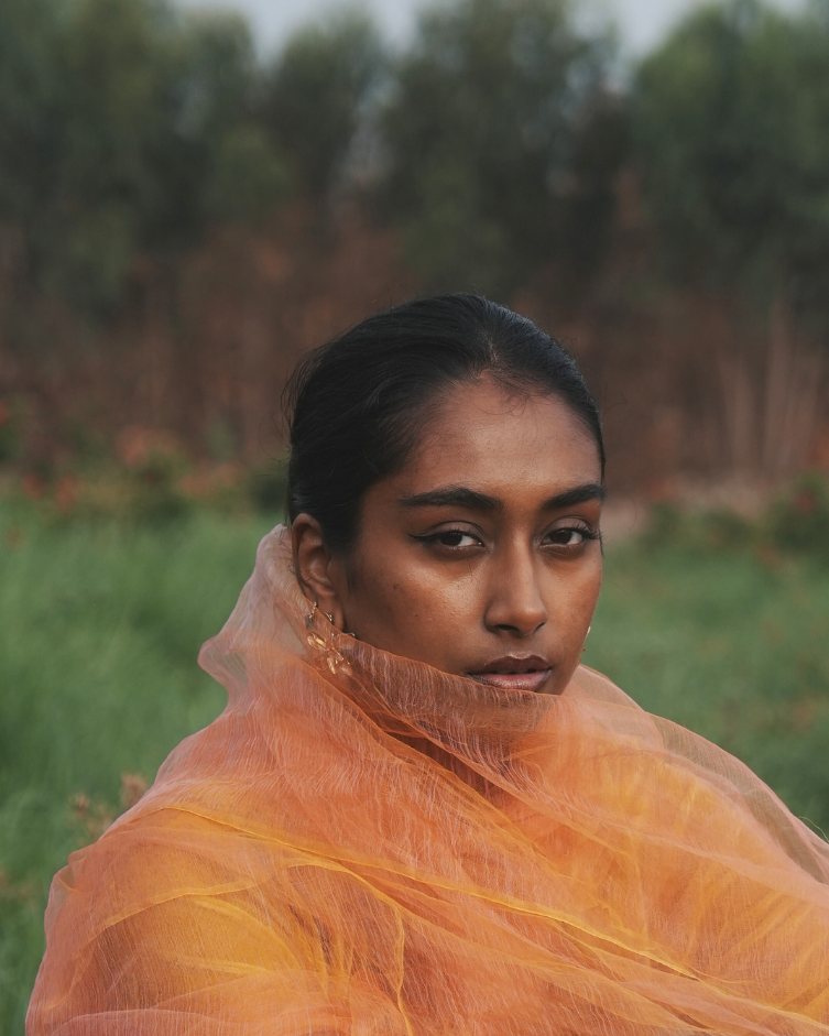 A model wrapped in the Sunburst Pink handwoven silk scarf, showcasing its feather-light texture and soft golden-pink hues. Crafted by skilled artisans using traditional techniques, this luxury silk scarf captures shifting light and timeless elegance, making it a versatile statement piece for any occasion.