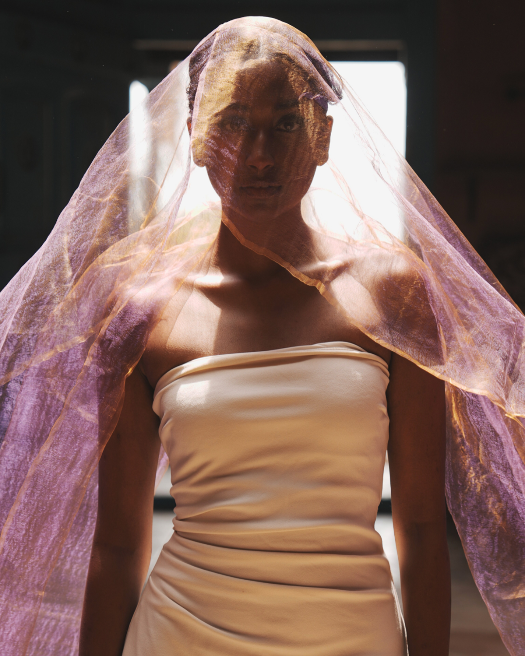 Model wearing the Sunburst Purple handwoven silk scarf as a luminous veil, showcasing its dual-tone blush and gold hues in soft natural light. Crafted in Phulia, West Bengal, this featherlight 19g artisan scarf embodies traditional weaving, slow fashion, and timeless Indian craftsmanship.