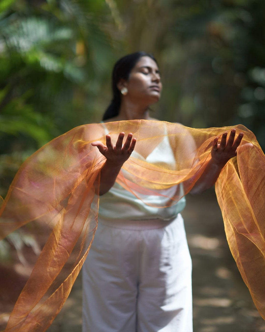 Woman holding an orange scarf in a forest setting