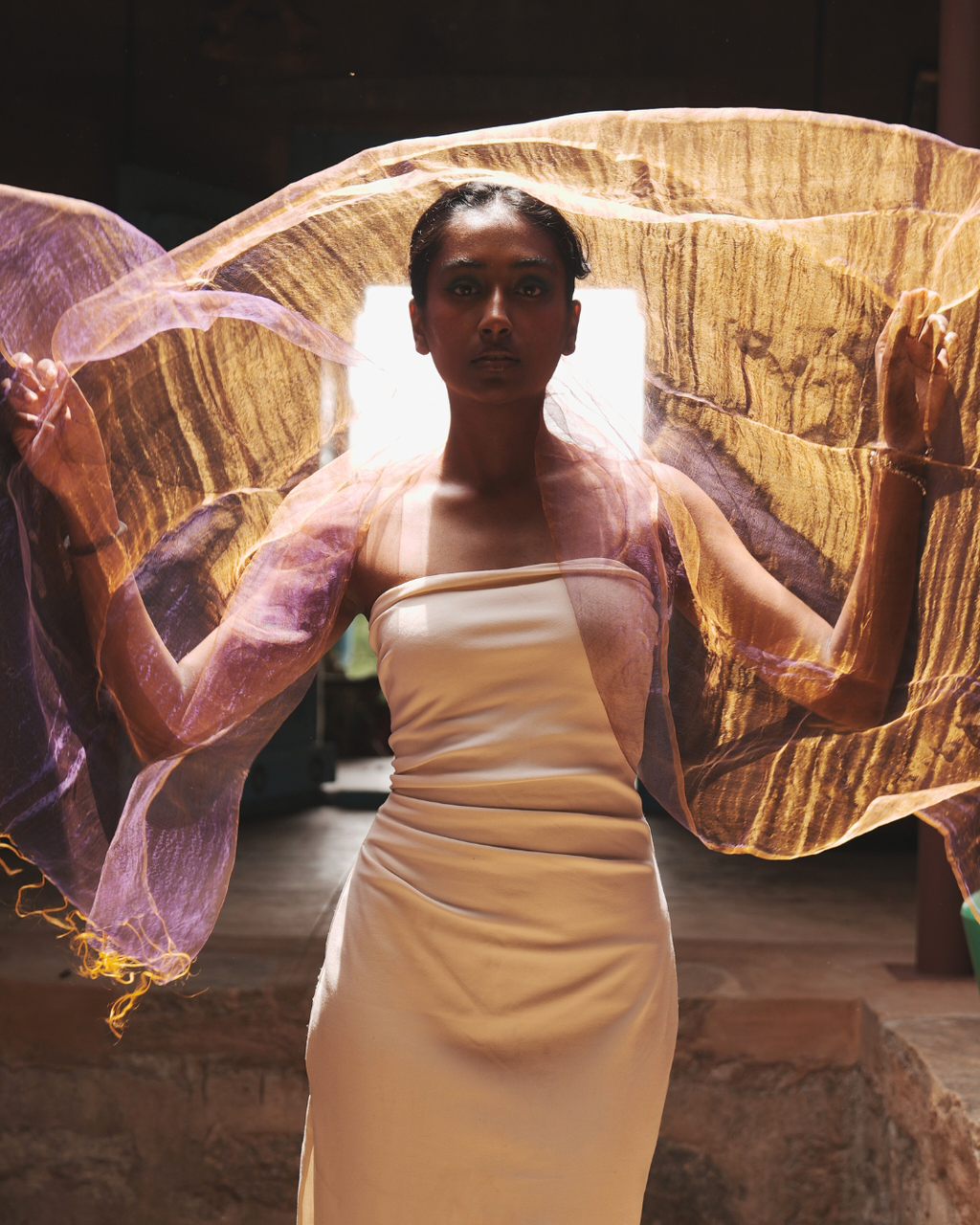 Model wearing the Sunburst Purple handwoven dual-tone silk scarf, showcasing its ethereal gold and purple hues as it catches the light in a sheer, weightless drape.