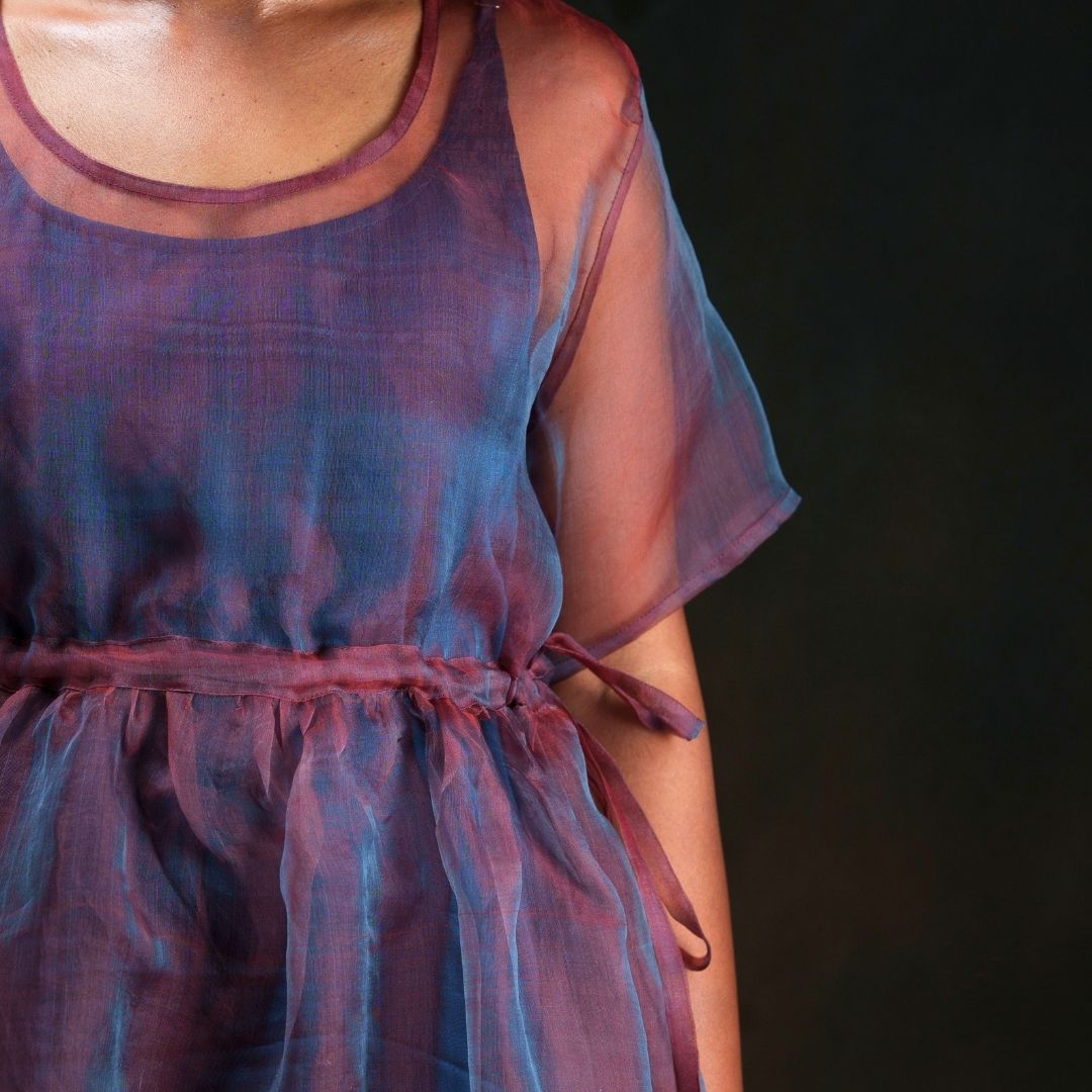 A close-up of a person wearing a blue and red dual tone sheer lightweight silk dress and dark blue inner featuring half sleeves and a side-tie waist.